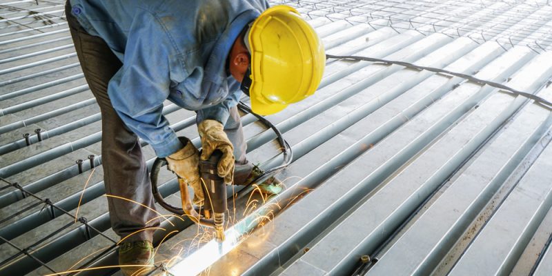 Man welds metal deck slab of mezzanine floor in construction industrial building