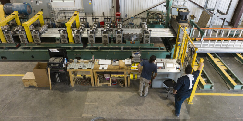 Two workers operate a steel deck roll-forming line inside CSM Metal Deck’s manufacturing facility.
